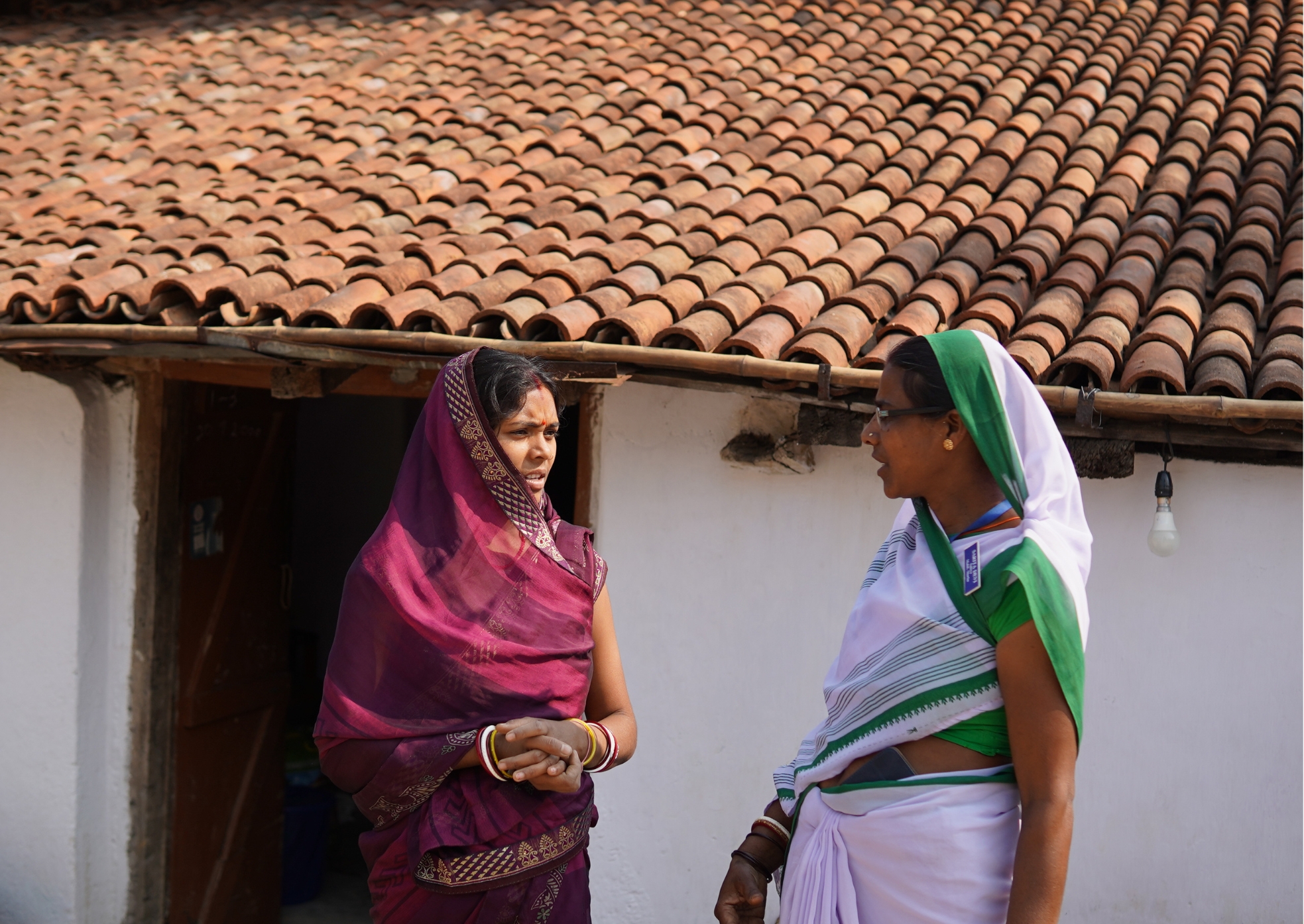 Sarita Devi speaking with a mother at her doorstep during a home visit in Khunti district