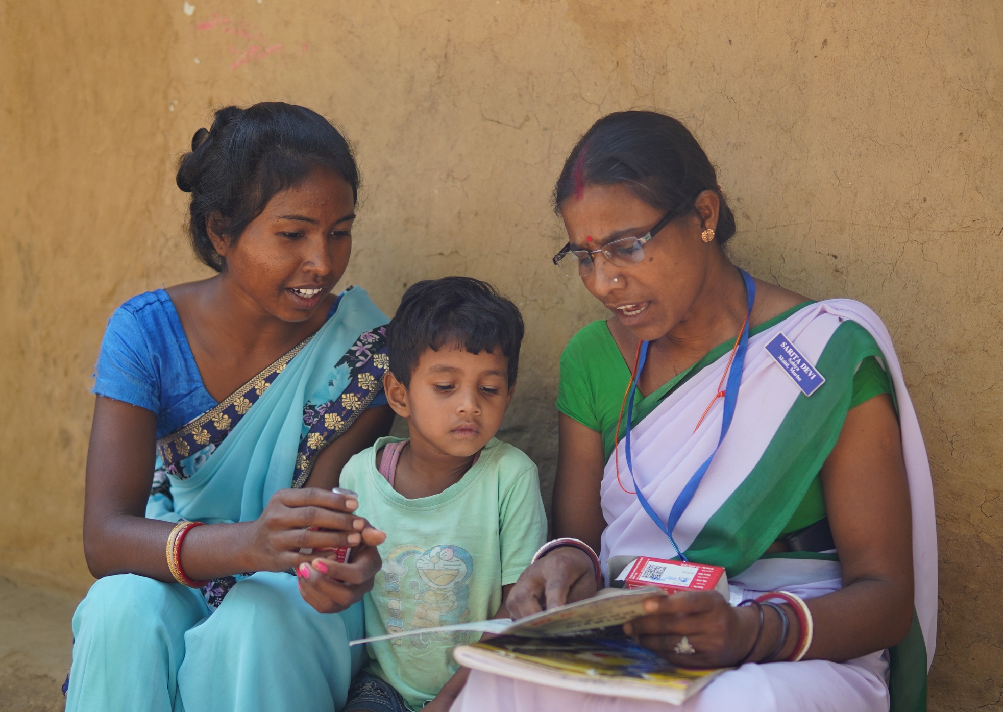 Sarita Devi with a mother and child, reviewing IFA supplementation materials during a home visit in Khunti