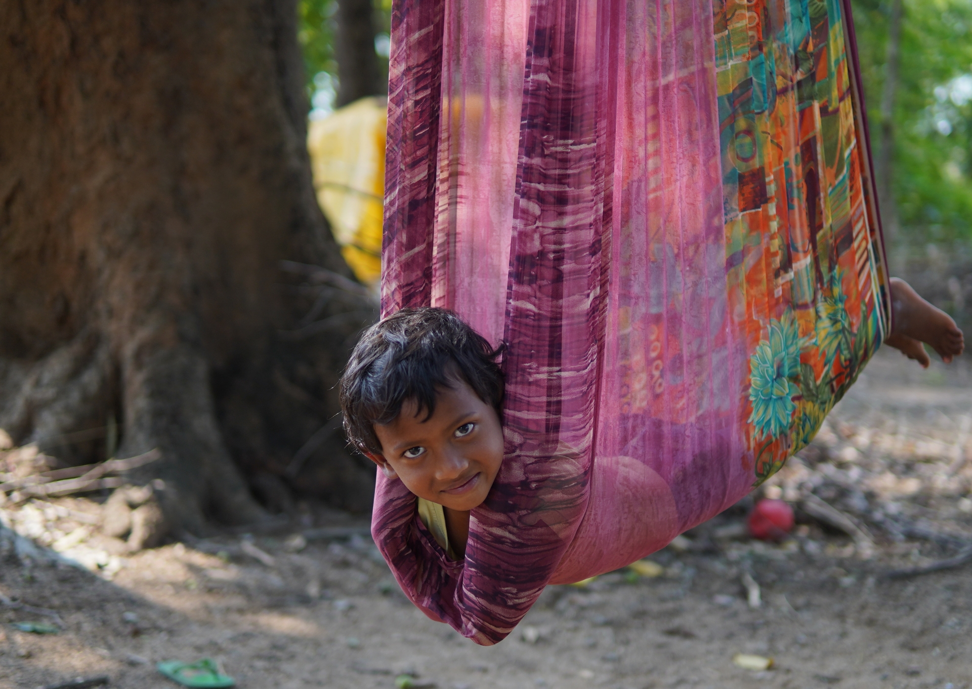 A young child playing in a hammock, smiling, in Khunti district