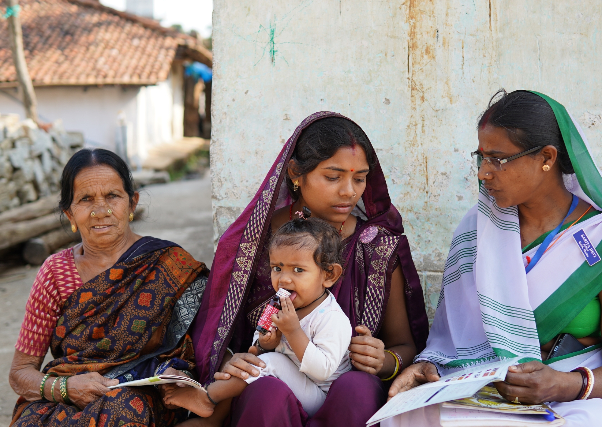 Sarita Devi with a mother, grandmother, and toddler receiving IFA syrup during a home visit in Khunti district